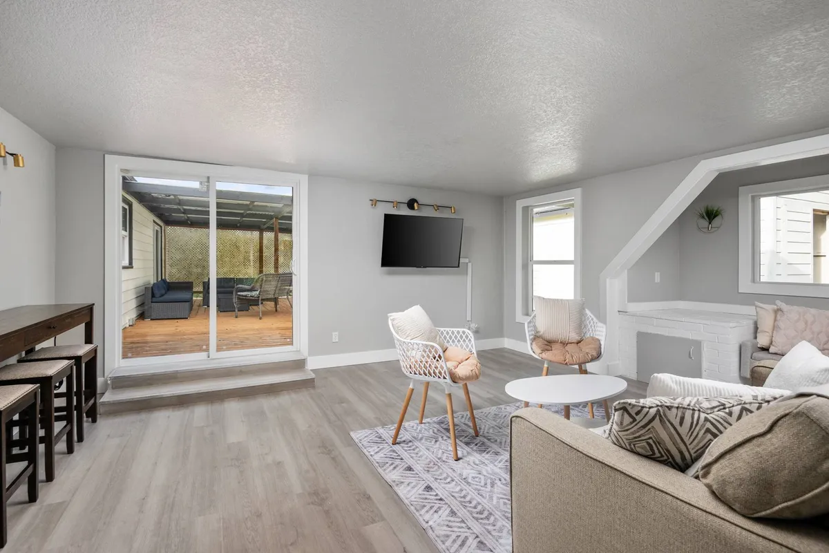 Featuring a comfortable sofa with patterned cushions, modern armchairs, and prominent sliding glass doors that open out to the deck, this image visually connects the indoor living area with the outdoor environment. The deck outside is partially visible, reinforcing indoor-outdoor living.