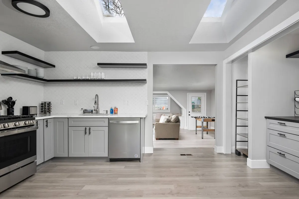 A bright, modern kitchen featuring stainless steel appliances, open shelving, skylights, and a functional island. The neutral color palette and updated décor create a fresh and contemporary environment ideal for preparing quick meals or hosting casual get-togethers.