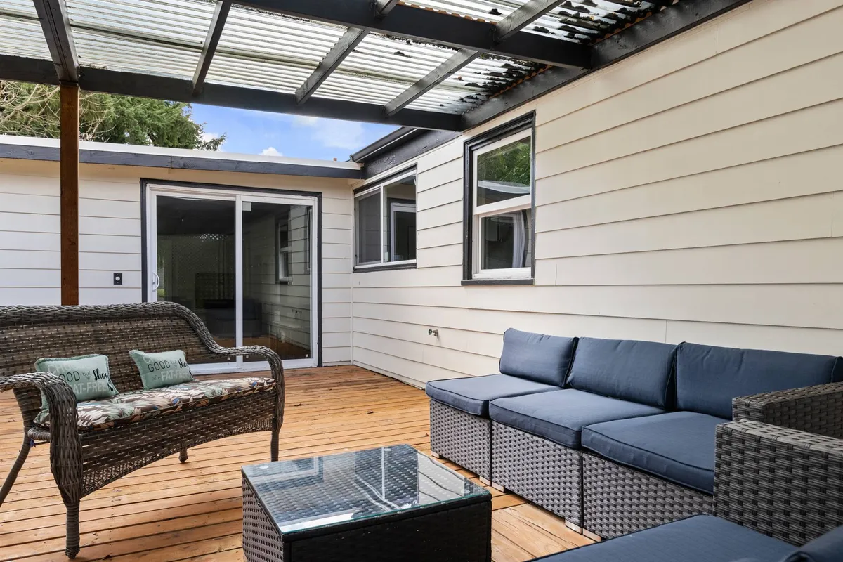 This image showcases a bright, comfortable interior living space with wicker seating, a glass coffee table, and abundant natural light streaming in through the glass roof. A sliding glass door hints at easy access to the backyard, inviting the outdoors in and promising a seamless indoor-outdoor experience.